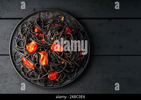 Spaghetti noirs avec tomates cerises sur planches noires. Pâtes noires cuites aux tomates rouges sur une assiette noire. Vue de dessus. Copier l'espace Banque D'Images