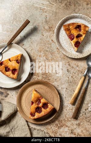 Morceaux de la tarte au gâteau au Plum du New York Times pour trois personnes sur fond texturé brun, vue de dessus, plat. Orientation verticale Banque D'Images