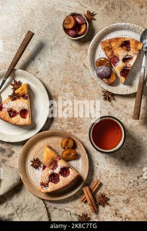 Morceaux de la tarte au gâteau au Plum du New York Times avec thé sur fond texturé brun, vue de dessus, plat. Orientation verticale Banque D'Images