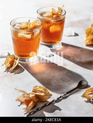 Cocktails de boisson froide saine orange décorés de baies physalis sur fond de marbre. Buvez une photo avec une lumière dure et des ombres claires. Fête d'automne Banque D'Images