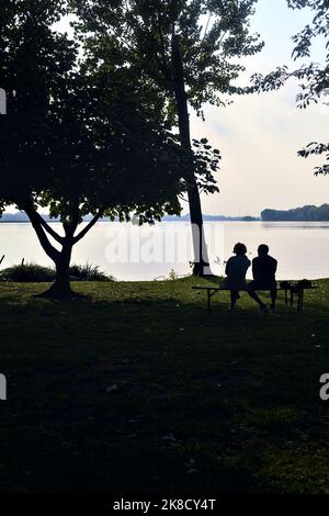 Couple assis sur un banc au bord du lac au coucher du soleil vu de loin Banque D'Images