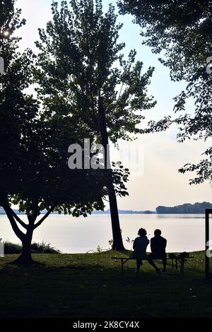 Couple assis sur un banc au bord du lac au coucher du soleil vu de loin Banque D'Images