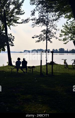 Couple assis sur un banc au bord du lac au coucher du soleil vu de loin Banque D'Images