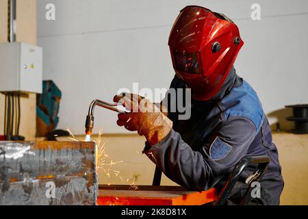 Le soudeur dans le masque coupe la poutre en acier avec le tuyau de soufflage de coupe dans l'atelier Banque D'Images