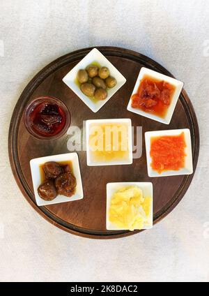 Sept plats de condiments avec confitures, olives et beurre disposés sur un plateau en bois et photographiés d'en haut à Berat, en Albanie. Banque D'Images