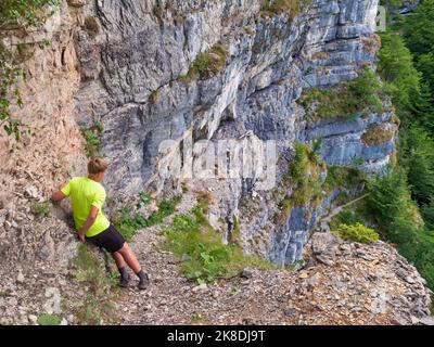 Garçon en chemise jaune regardant vers le bas de la voie avec chaîne en acier ancrée dans le mur rocailleux, chemin via le style ferrata. Nom du chemin en Italie Sentieri Attrezzat Banque D'Images