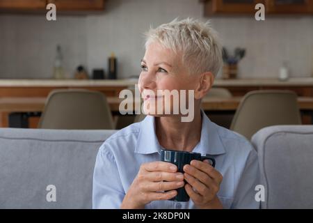 Une femme heureuse et âgée se détendant sur un canapé avec une tasse Banque D'Images