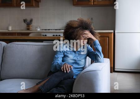 Une adolescente africaine malheureuse pleure assise seule sur le canapé Banque D'Images