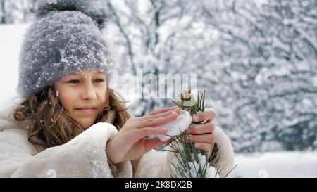 Décoration extérieure arbre de Noël. Cutie, jolie petite fille décore l'arbre de Noël recouvert de neige avec des jouets de glace faits maison, pendant la neige, en forêt. Happy time par jour d'hiver enneigé. Activités familiales en plein air en hiver. Ralenti. Photo de haute qualité Banque D'Images