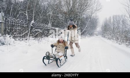 en hiver, en famille, en plein air. Les enfants sont heureux, rires et ludiques. Ils s'amusent sur une route enneigée, en forêt ou en chute de neige. Les enfants s'amusent par une journée hivernale enneigée. Ralenti. Photo de haute qualité Banque D'Images