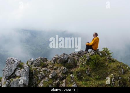 Randonneur, âgé de 63 ans, reposant sur le Leonhardstein dans le brouillard, Kreuth, Mangfall Mountains, haute-Bavière, Allemagne Banque D'Images