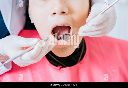 Dentiste vérifiant la bouche du patient à l'aide d'un miroir dentaire. Gros plan du patient vérifié par le dentiste, gros plan des mains du dentiste vérifiant la bouche du patient Banque D'Images