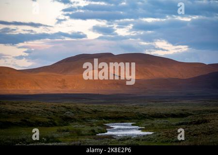 Collines illuminées rouges au coucher du soleil, paysage volcanique, rivière passant par les prairies, Moeorudalur, montagnes islandaises, Islande Banque D'Images