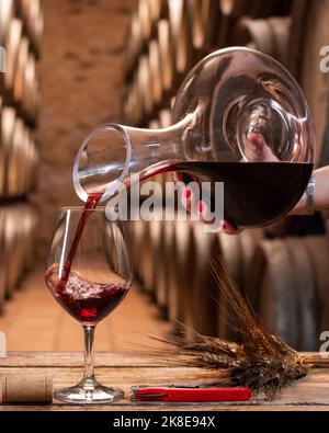 Cave de vinification. Verser le vin rouge du décanter dans le verre à vin pour dégustation, sur une table rustique en bois. Boisson, alcool. Banque D'Images