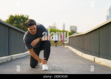 Asian Runner souffrant de blessures à la cheville après un sport en plein air dans un parc de la périphérie de la ville Banque D'Images