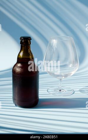 Vue de dessus de la bouteille de bière brune en verre, verre de bière sur fond bleu gros plan. Mode de vie de la nourriture. Production de boissons alcoolisées. Copier l'espace, maquette. Banque D'Images