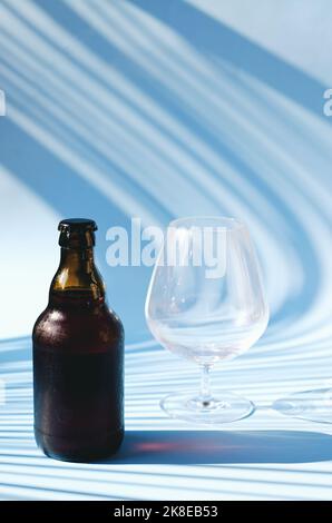 Vue de dessus de la bouteille de bière brune en verre, verre de bière sur fond bleu gros plan. Mode de vie de la nourriture. Production de boissons alcoolisées. Copier l'espace, maquette. Banque D'Images