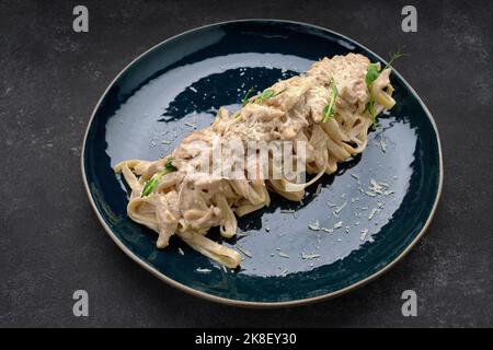 Pâtes avec poulet, champignons et fromage, sur une assiette, sur fond sombre Banque D'Images