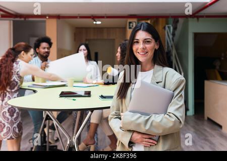 Portrait d'une femme d'affaires souriante brune tenant un ordinateur portable au bureau Banque D'Images