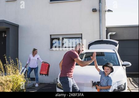 Un père et un fils heureux qui se trouvent devant une voiture électrique Banque D'Images