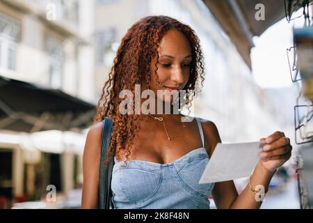 Jeune femme souriante aux cheveux bouclés regardant une carte postale Banque D'Images