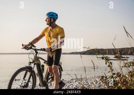Homme portant un casque de vélo marchant avec un vélo à la plage Banque D'Images