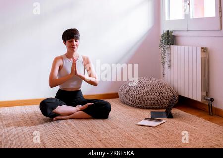 Femme assise avec les yeux fermés pratiquant le yoga à l'aide d'un Tablet PC à la maison Banque D'Images