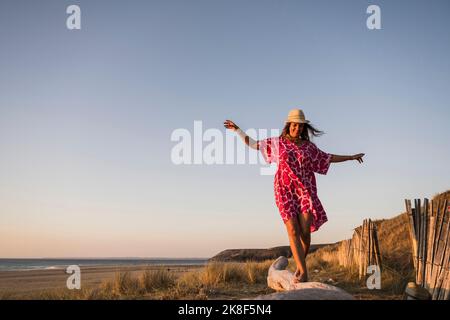 Bonne femme mûre avec les bras débordés marchant sur le bois à la plage Banque D'Images