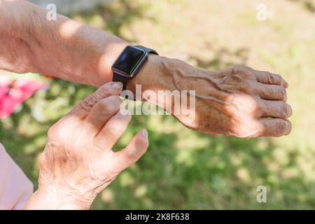 Mains d'une femme âgée portant une montre intelligente par beau temps Banque D'Images
