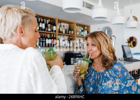 Femme d'affaires mature avec un ami, sirotant un cocktail au bar Banque D'Images