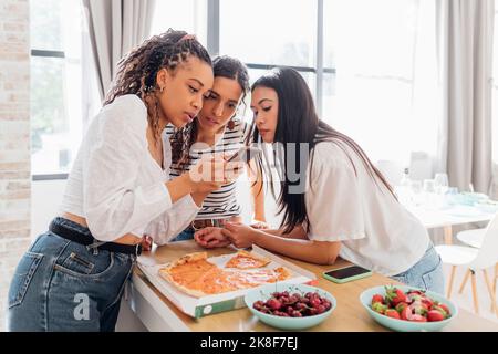 Femme partageant un smartphone avec des amis dans la cuisine à la maison Banque D'Images