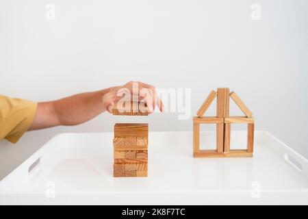 Main de l'homme construire la maison modèle avec des blocs de jouets sur la table basse Banque D'Images