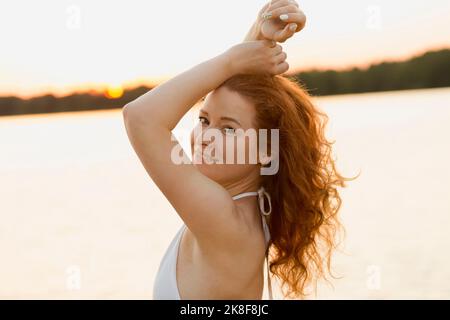 Femme souriante devant l'eau au coucher du soleil Banque D'Images