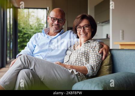 Heureux couple senior portant des lunettes de vue assis ensemble à la maison Banque D'Images