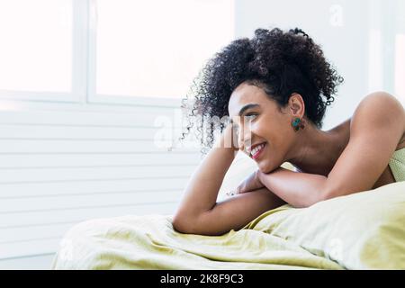 Femme attentionnés avec des cheveux bouclés couchés sur le lit à la maison Banque D'Images