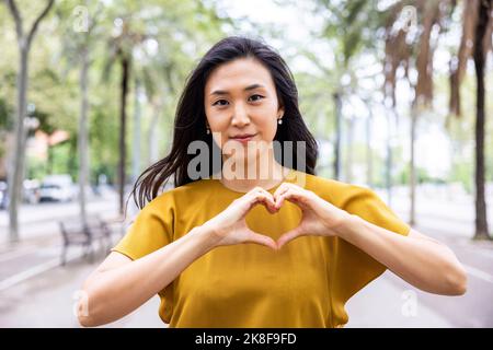 Femme souriante en forme de coeur avec les mains sur le sentier Banque D'Images