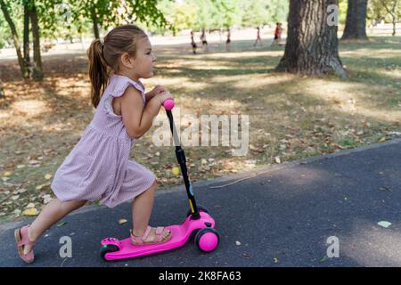 Une jeune fille qui s'appuie sur un scooter de poussée sur une piste de marche au parc Banque D'Images