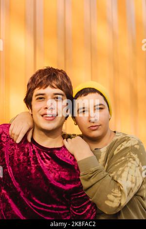 Heureux couple non binaire debout ensemble devant le mur ondulé jaune Banque D'Images