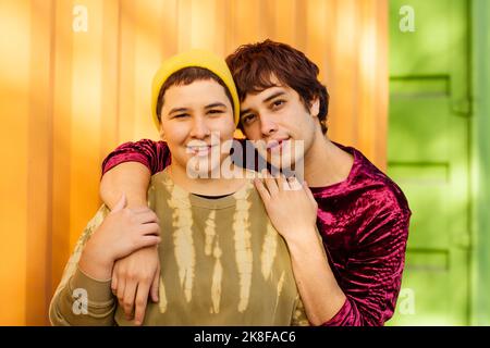 Couple non binaire souriant debout devant un conteneur de cargaison jaune Banque D'Images