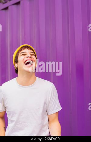 Une personne joyeuse et non binaire riant devant le mur violet Banque D'Images