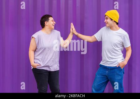 Couple non binaire heureux donnant cinq haut en face de la paroi ondulée Banque D'Images