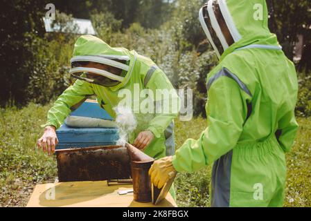 Apiculteur avec un collègue tenant un fumeur d'abeille examinant la ruche à apiary Banque D'Images