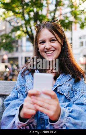 Bonne femme portant une veste en denim tenant un téléphone portable Banque D'Images