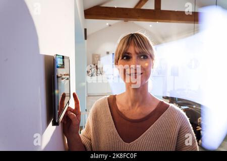 Femme utilisant une application d'automatisation domestique intelligente via une tablette PC au mur à la maison Banque D'Images