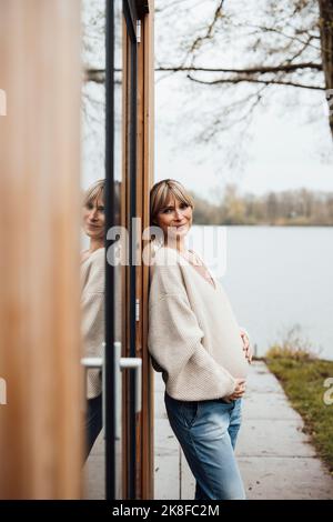 Femme souriante touchant le ventre de la femme enceinte en se penchant sur la porte Banque D'Images