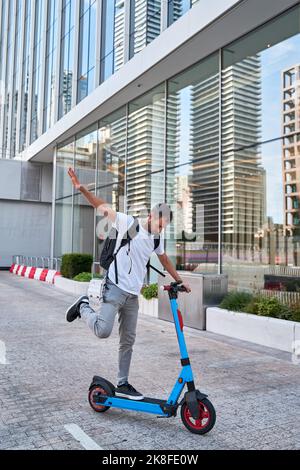 Homme à la main levée d'équilibrage sur un scooter électrique de poussée devant les bâtiments Banque D'Images