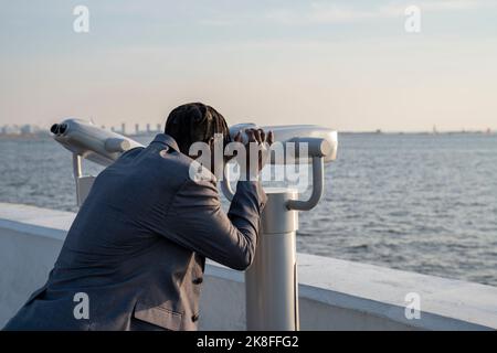 Homme d'affaires regardant à travers des jumelles à pièces au coucher du soleil Banque D'Images