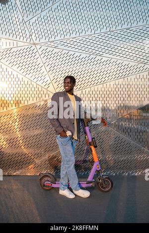 Homme d'affaires souriant avec scooter électrique sur la piste de marche Banque D'Images