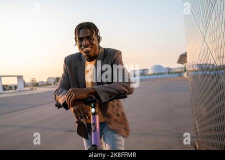 Un jeune homme d'affaires heureux avec un scooter électrique dans la rue Banque D'Images