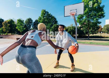 Un sportif souriant jouant au basket-ball avec un ami sur un terrain de sport Banque D'Images